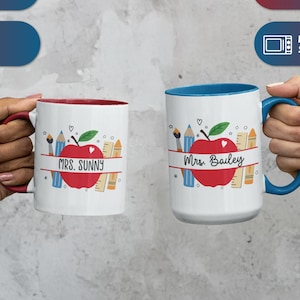 May include: Two white ceramic mugs with teacher-themed designs. One mug has a red interior and handle, the other has a blue interior and handle. Each mug features a red apple, pencils, and the name of a teacher.