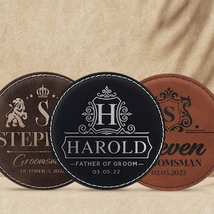 May include: Three round leather coasters with personalized engravings. The coasters are brown, black, and brown with gold lettering. The text on the coasters reads "STEPI Groomsm OCTOBER 3, 20%", "HAROLD -FATHER OF GROOM- 03.05.22", and "even OMSMAN 02.05.2022".