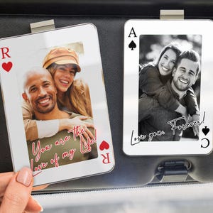 May include: Two playing card-shaped photo car visor clips. One features a color photo with the text "You are the love of my life!" and a red heart. The other has a black and white photo with the text "Love you Forever!" and a spade.