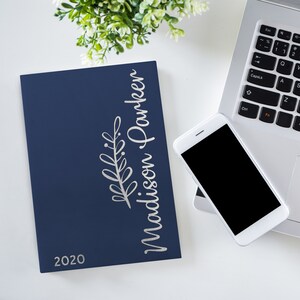 May include: A navy blue 2020 planner with silver foil lettering that reads "Madison Parker" and a silver foil branch design.
