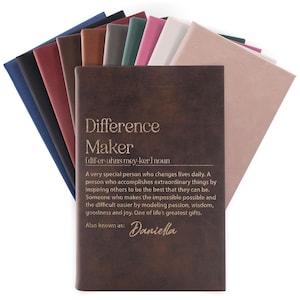May include: A collection of leather-bound journals in various colors, including navy, burgundy, and brown. The front journal is embossed with the words "Difference Maker" and a definition. The name "Daniella" is also included.
