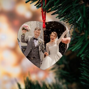 May include: A heart-shaped ornament with a photo of a bride and groom exiting a ceremony. The couple is smiling and holding hands as they walk down the aisle. Confetti is falling around them.
