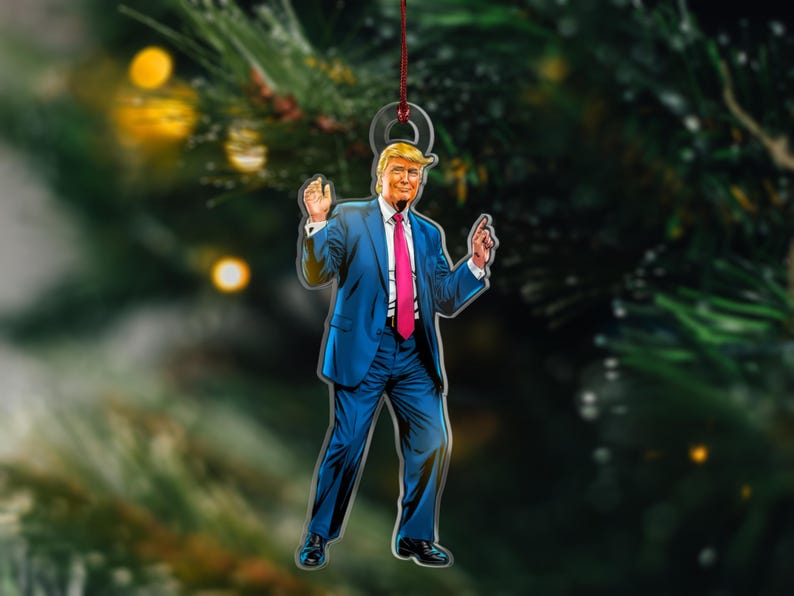 May include: A Christmas ornament featuring a cartoon illustration of a man in a blue suit and pink tie, with a red string for hanging.