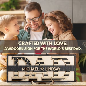 May include: A wooden sign with the text "CRAFTED WITH LOVE, A WOODEN SIGN FOR THE WORLD'S BEST DAD." The sign is decorated with an American flag pattern and the words "DAD" are in large, bold letters. The sign also includes the names "MICHAEL" and "LINDSAY" in smaller letters.