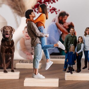 May include: Photo cutouts of a dog, a couple, a baby, and a family, each mounted on a wooden base. The couple is embracing, the family is smiling, and the dog is a chocolate lab. The baby is sitting.