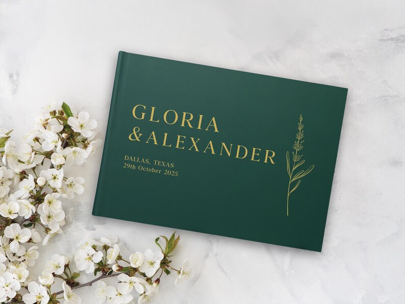 Puede incluir: Un libro de visitas de boda verde oscuro con letras doradas que dice "GLORIA & ALEXANDER" y la fecha "29 de octubre de 2025". Una ilustraci&oacute;n floral est&aacute; en el lado derecho. Flores blancas en el fondo.