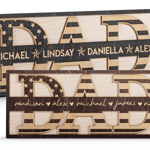 May include: Two wooden signs with the word "DAD" in large letters. The letters are decorated with an American flag pattern. The signs have a brown border and a smaller banner below the letters with names and symbols. The top sign has the names "MICHAEL", "LINDSAY", "DANIELLA", and "ALEX" with stars between each name. The bottom sign has the names "madison", "alex", "michael", "james", and "noah" with hearts between each name.