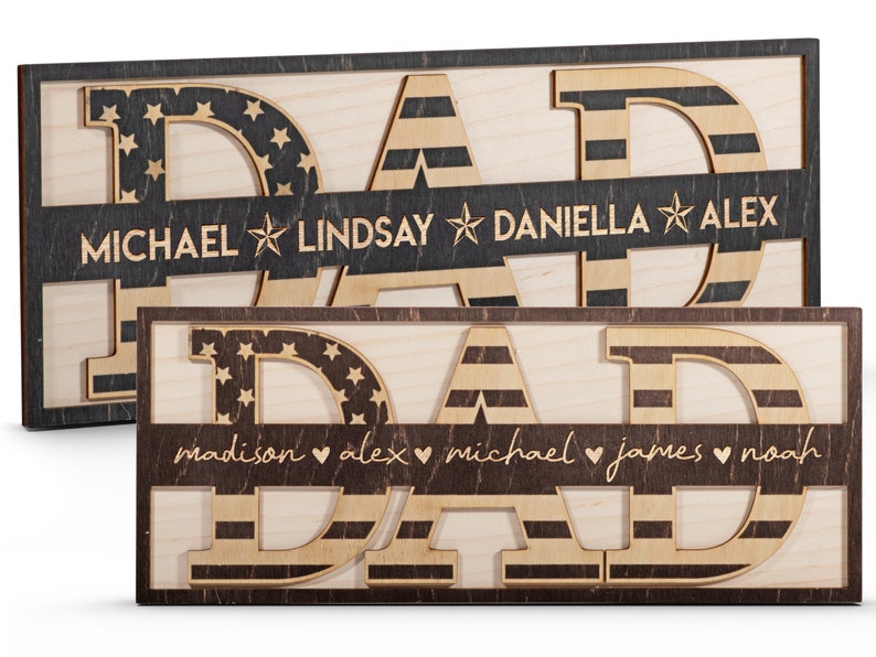 May include: Two wooden signs with the word "DAD" in large letters. The letters are decorated with an American flag pattern. The signs have a brown border and a smaller banner below the letters with names and symbols. The top sign has the names "MICHAEL", "LINDSAY", "DANIELLA", and "ALEX" with stars between each name. The bottom sign has the names "madison", "alex", "michael", "james", and "noah" with hearts between each name.