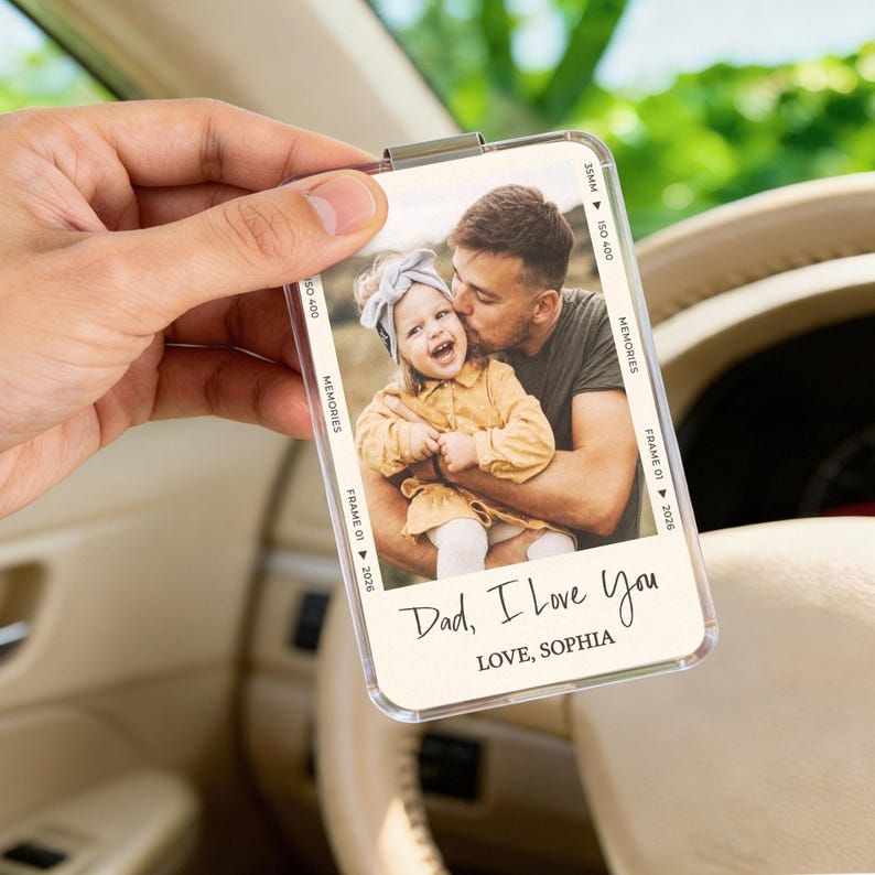 May include: A clear acrylic photo holder with a photo of a father kissing a young child. The photo has a vintage film strip border with the text "Dad, I Love You" and "LOVE, SOPHIA". The holder is held in a hand.
