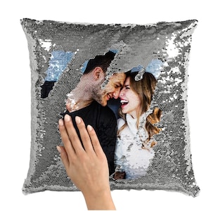 May include: A silver sequin pillow with a hidden photo of a couple smiling at each other. The photo is revealed by flipping the sequins.