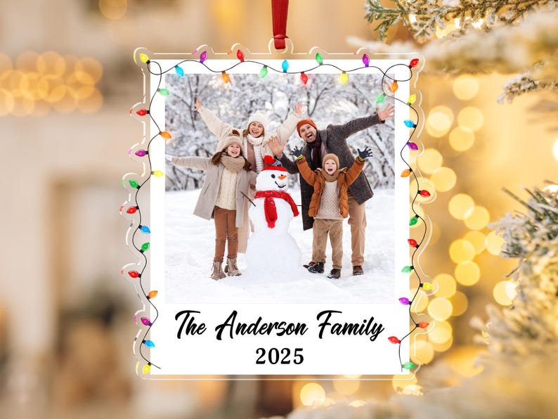 Pode incluir: Enfeite de Natal em acr&iacute;lico transparente com uma foto de fam&iacute;lia no interior, emoldurado por uma sequ&ecirc;ncia de luzes coloridas. A foto mostra uma fam&iacute;lia de quatro pessoas com um boneco de neve em um cen&aacute;rio de neve. O texto diz "The Anderson Family 2025."