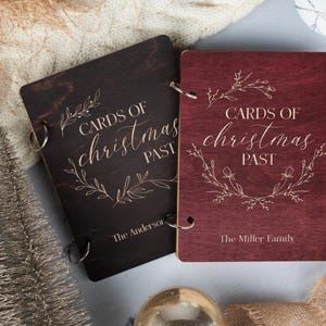 May include: Two wooden photo albums with a burgundy and black finish. The albums are decorated with a floral design and the text "Cards of Christmas Past". The albums are personalised with the names "The Anderson" and "The Miller Family".