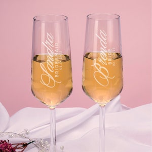 Puede incluir: Dos copas de champ&aacute;n transparentes llenas de un l&iacute;quido dorado. Las copas est&aacute;n personalizadas con texto blanco: "Sandra, Dama de honor, 02.17.2022" y "Brenda, Novia, 02.17.2022". El fondo es rosa suave.