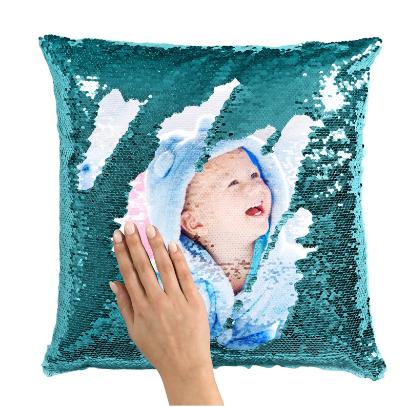 May include: Teal sequin pillow with a photo of a baby in a blue and white outfit. The sequins can be flipped to reveal a different color.