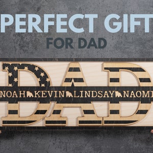 May include: Wooden sign with the word "DAD" in large letters, each letter decorated with an American flag design. A smaller banner below reads "NOAH KEVIN LINDSAY NAOMI".