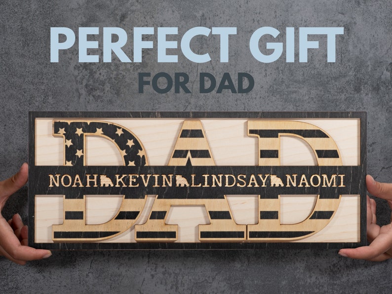 May include: Wooden sign with the word "DAD" in large letters, each letter decorated with an American flag design. A smaller banner below reads "NOAH KEVIN LINDSAY NAOMI".