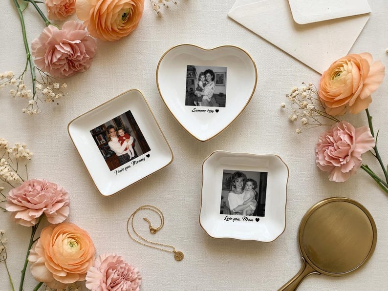 May include: Three white ceramic trinket dishes with gold-toned rims, each featuring a black and white photograph and printed text. One heart-shaped dish reads Summer 1996, one square dish reads I love you, Mommy, and one square dish reads Love you, Mom.