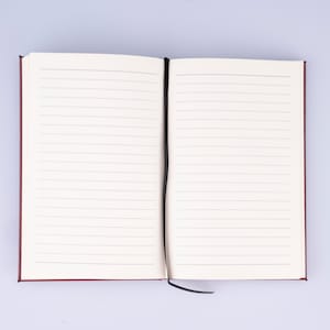 May include: A burgundy notebook with a black ribbon bookmark. The notebook is open to a blank page with lined paper.