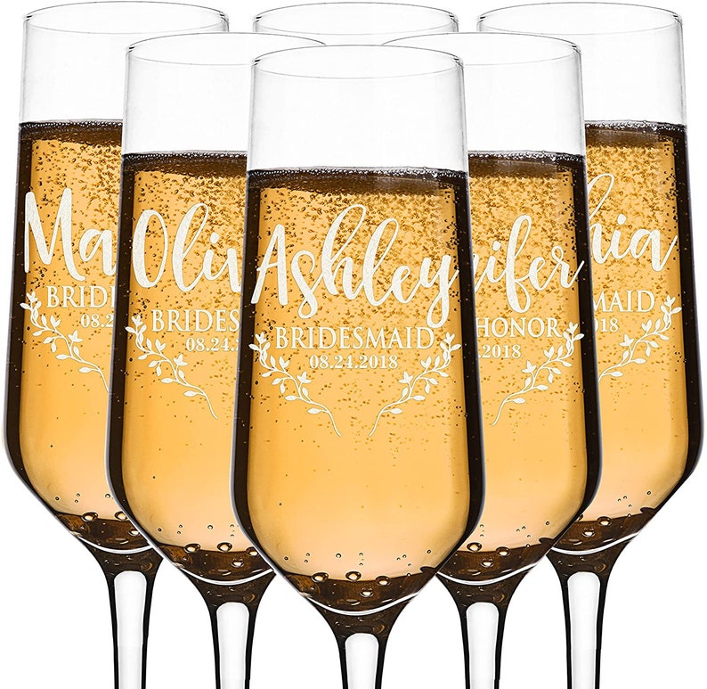 Puede incluir: Seis copas de champ&aacute;n llenas de un l&iacute;quido dorado brillante. Cada copa est&aacute; personalizada con un nombre, un rol y una fecha en una fuente blanca, con detalles florales. Las copas son para una boda.