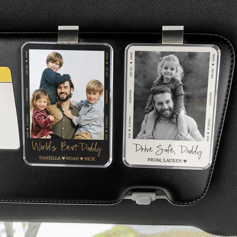 May include: Two rectangular car visor photo holders with family photos. One says "World's Best Daddy" with names below. The other says "Drive Safe, Daddy" with a name below. Both have a metal clip.