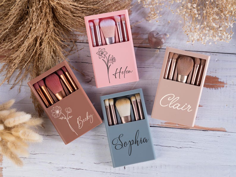 May include: Four personalized makeup brush sets in pink, brown, beige, and blue. Each set includes several brushes and a larger brush, all in a matching case. The cases are decorated with floral designs and names: Helen, Becky, Clair, and Sophia.