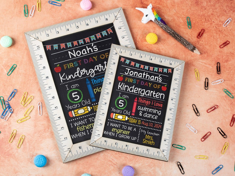 Puede incluir: Dos letreros de pizarra negra con marcos de madera blanca y bordes de regla. Los letreros est&aacute;n decorados con acentos coloridos y anuncian "Noah's First Day of Kindergarten" y "Jonathan's First Day of Kindergarten". Los letreros incluyen detalles como la edad, las cosas favoritas y las aspiraciones futuras.