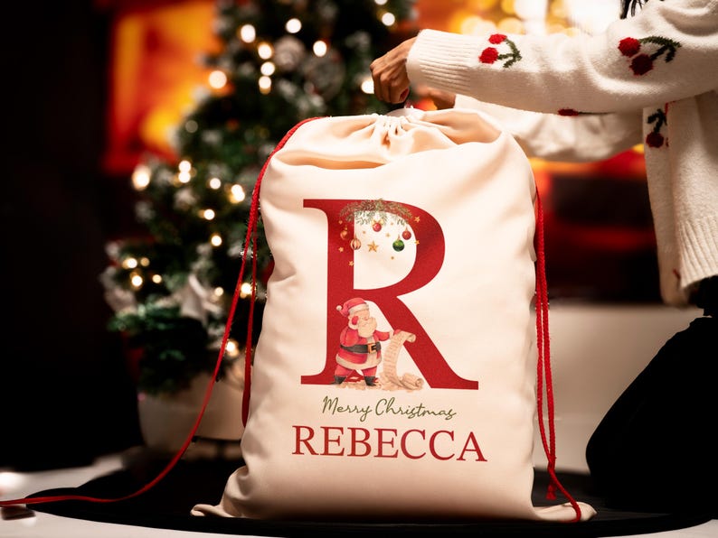 May include: A white Christmas stocking with a red letter R, a Santa Claus illustration, and the text "Merry Christmas REBECCA".