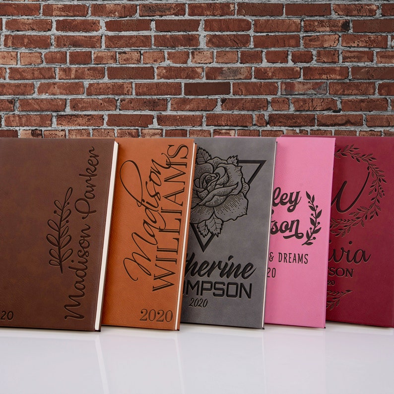 May include: Five personalized leather journals with different designs and names. The journals are brown, orange, gray, pink, and burgundy. The names on the journals are Madison Parker, Madison Williams, Catherine Simpson, Hayley, and Olivia. The year 2020 is printed on each journal.