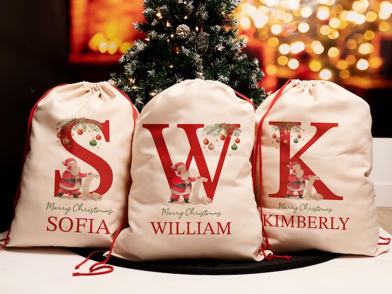 May include: Three personalized Christmas gift bags with red and white drawstring closures. Each bag features a large red letter, a Santa Claus illustration, and the text "Merry Christmas" with a name below. The names are Sofia, William, and Kimberly.