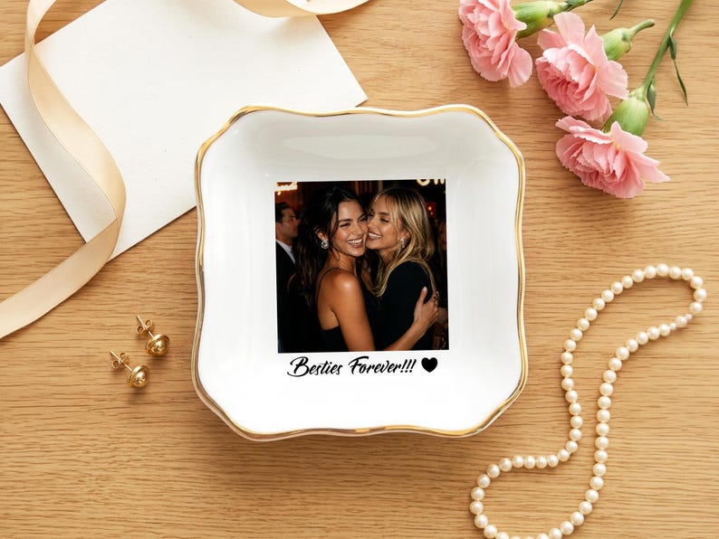 May include: A square white ceramic trinket dish with a gold-trimmed scalloped edge. The center features a printed photograph of two smiling people embracing, with the black text "Besties Forever!!!" and a small black heart icon printed below.