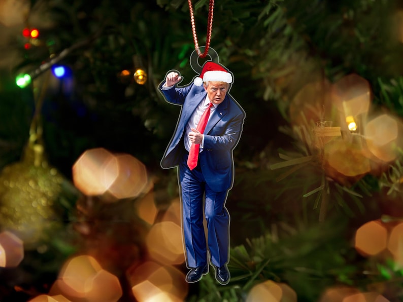 May include: A Christmas ornament featuring a person wearing a blue suit, red tie, and a Santa hat. The ornament is hanging from a Christmas tree.