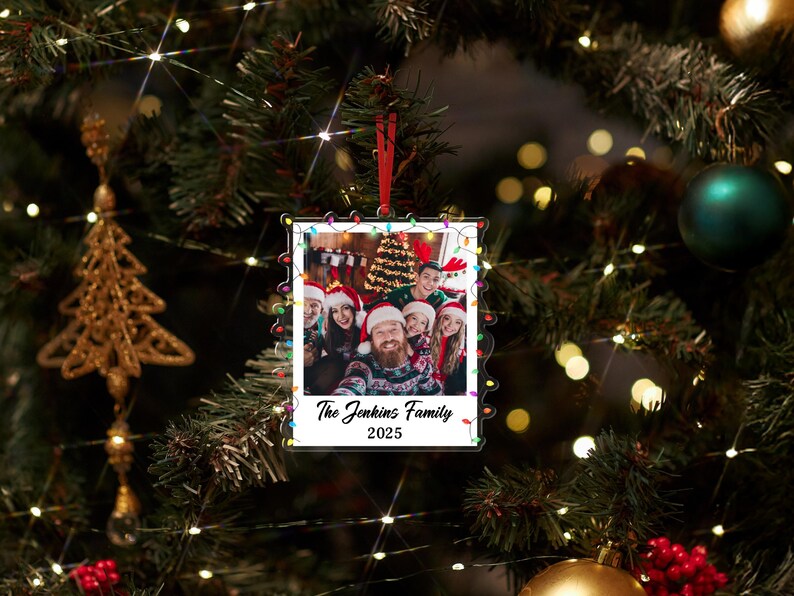 Pode incluir: Enfeite de Natal em acr&iacute;lico transparente com uma foto de fam&iacute;lia no interior, rodeado por uma s&eacute;rie de luzes coloridas. A foto mostra um grupo de pessoas com gorros de Pai Natal. O texto no enfeite diz "The Jenkins Family 2025".