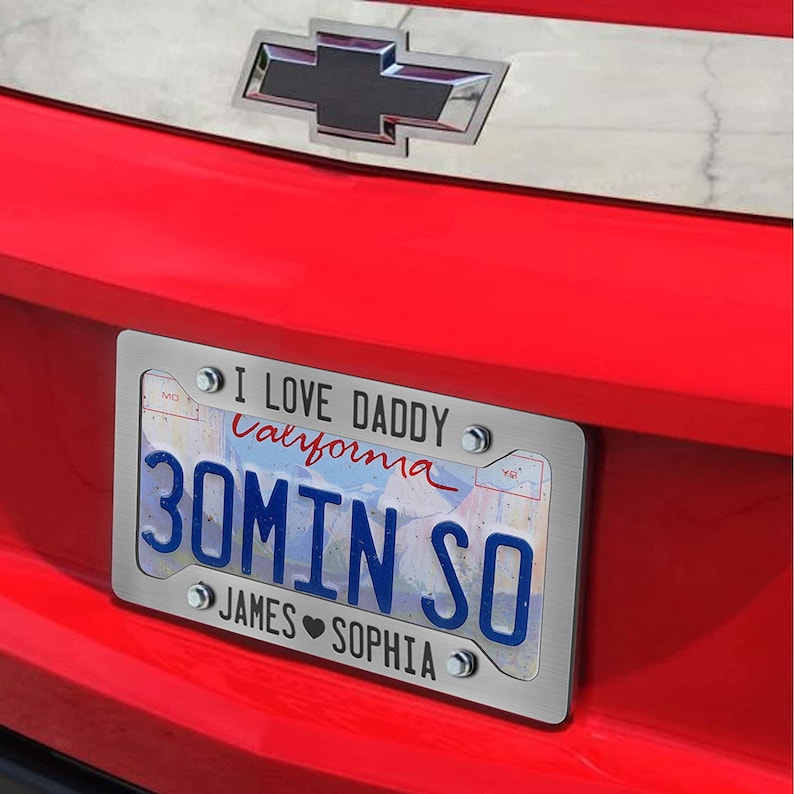 Puede incluir: Una placa de matr&iacute;cula personalizada de plata con el texto "I Love Daddy California 30min So James Sophia" y una imagen de fondo azul y blanco. La placa est&aacute; unida a un coche rojo.