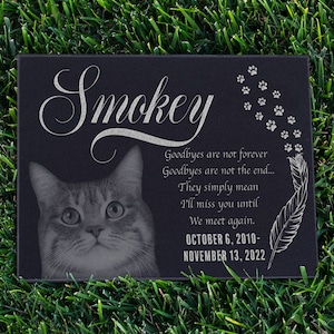 May include: Black granite pet memorial with a photo of a tabby cat and the inscription "Smokey". The inscription also includes the text "Goodbyes are not forever, Goodbyes are not the end... They simply mean I'll miss you until We meet again. October 6, 2010 - November 13, 2022".