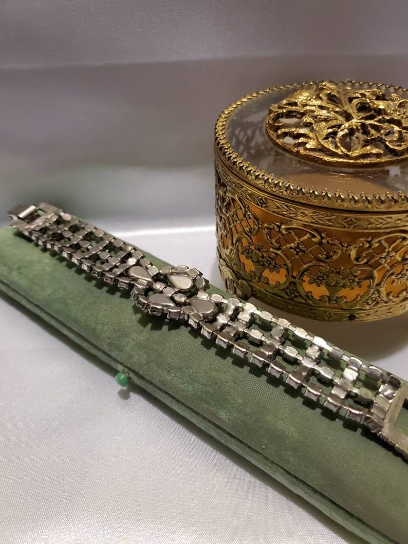 May include: A silver rhinestone bracelet with a large, ornate rhinestone cluster in the center. The bracelet is lying on a green velvet box.