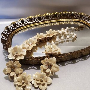 May include: A white floral necklace with rhinestone accents. The necklace is on a gold mirrored tray.