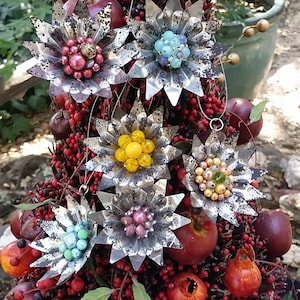 May include: A Christmas tree made of twigs and berries is decorated with six handmade ornaments. The ornaments are made of metal and have a star shape. Each star is adorned with a cluster of colorful beads in the center. The beads are red, blue, yellow, green, and pink.