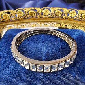 May include: A silver bangle bracelet with a row of clear rectangular crystals.
