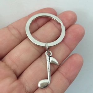 May include: Silver key ring with a music note charm. The key ring is attached to a silver ring.