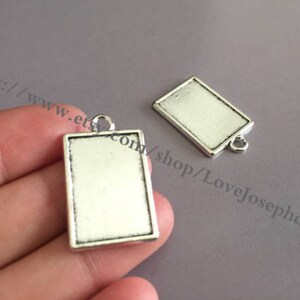 Puede incluir: Dos bandejas de colgantes de metal plateadas con forma rectangular y un bucle en la parte superior para colgar. Las bandejas están en blanco y listas para la elaboración.