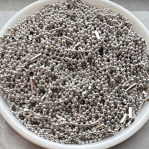 May include: A white bowl filled with a large quantity of silver ball chain. The chain is made of small, round metal beads connected by thin links.