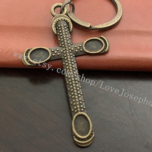 Op de afbeelding: Een bronzen sleutelhanger in de vorm van een kruis met een gedetailleerd ontwerp. Het kruis heeft een getextureerd oppervlak en een ring aan de bovenkant om sleutels aan te bevestigen.