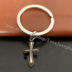May include: Silver key chain with a silver cross charm. The cross has a detailed design with small embellishments.