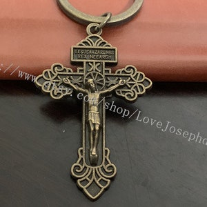 May include: A bronze-coloured metal cross with a figure of Jesus Christ on it. The cross has a decorative design and the inscription "EESUS NAZARENUS REX IUDEORUM" is on the top.