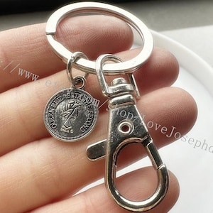 May include: Silver keyring with a round charm featuring a profile of Queen Elizabeth II and the text "Queen Elizabeth II 1952 Second". The keyring has a silver lobster clasp.