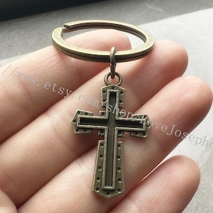May include: A bronze-colored cross keychain with a detailed design. The cross is attached to a simple metal ring.