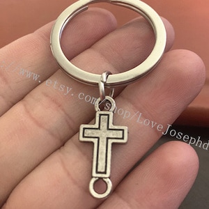 May include: Silver key chain with a silver cross charm. The cross has a simple design with a loop at the bottom.