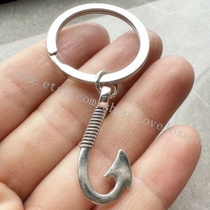 Puede incluir: Llavero de plata con un dije en forma de gancho. El gancho está detallado con un diseño texturizado.