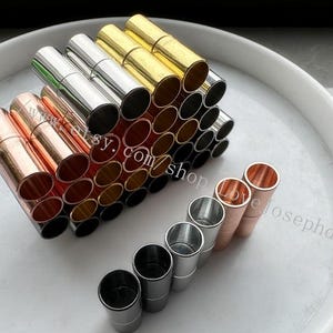 May include: A collection of metal magnetic clasps in various colors, including gold, silver, and copper. The clasps are arranged in a pyramid shape, with the smaller clasps at the top and the larger clasps at the bottom. There are also a few clasps in a row on the bottom of the image.