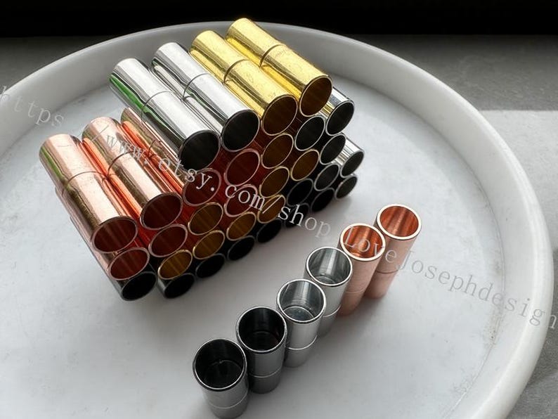 May include: A collection of metal magnetic clasps in various colors, including gold, silver, and copper. The clasps are arranged in a pyramid shape, with the smaller clasps at the top and the larger clasps at the bottom. There are also a few clasps in a row on the bottom of the image.